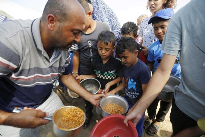 パレスチナ自治区ガザ南部ハンユニスの難民キャンプで国連の担当者から食事を受け取る子どもら　2023年10月24日　（ゲッティ＝共同）