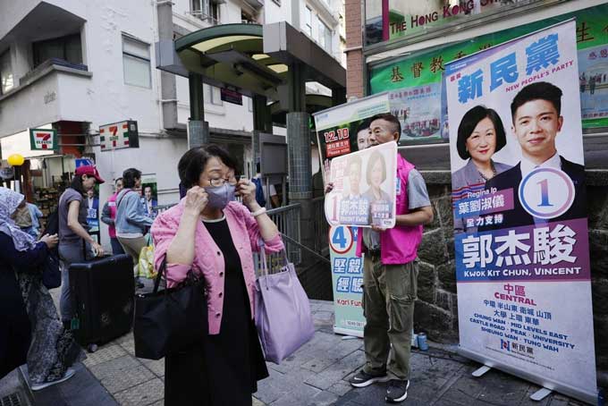 区議会選の候補者のポスターの前を通り過ぎる市民ら＝2023年12月10日、香港（共同）