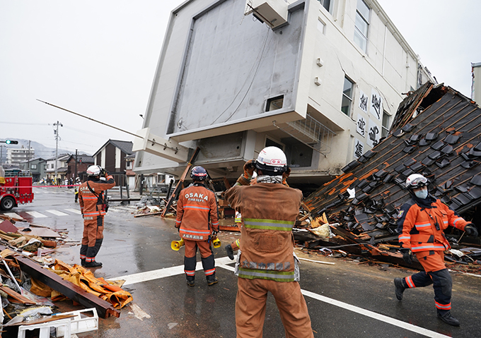 余震が発生し、救助活動中のビル倒壊現場から急いで退避する消防隊員ら＝2024年1月3日午後0時54分、石川県輪島市（恵守乾撮影）　写真提供：産経新聞社