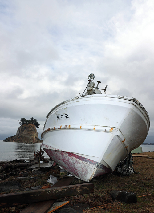 【能登半島地震】地震の影響で崩れた見附島（左奥）と打ちあがった漁船＝2024年2月7日午後、石川県珠洲市（鴨志田拓海撮影）　写真提供：産経新聞社