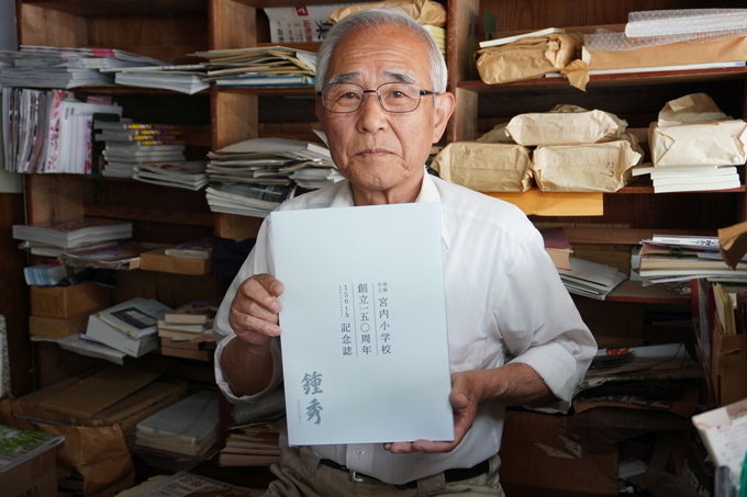 「佐野書店」の建物にあったという宮内小学校の150周年記念誌を手にする佐野憲一さん