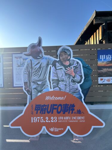 「甲府UFO事件」の現場に設置された、宇宙人に肩を叩かれる「顔はめパネル」と徳タケ喜一さん（写真提供：一般社団法人「UFOKOFU1975」）