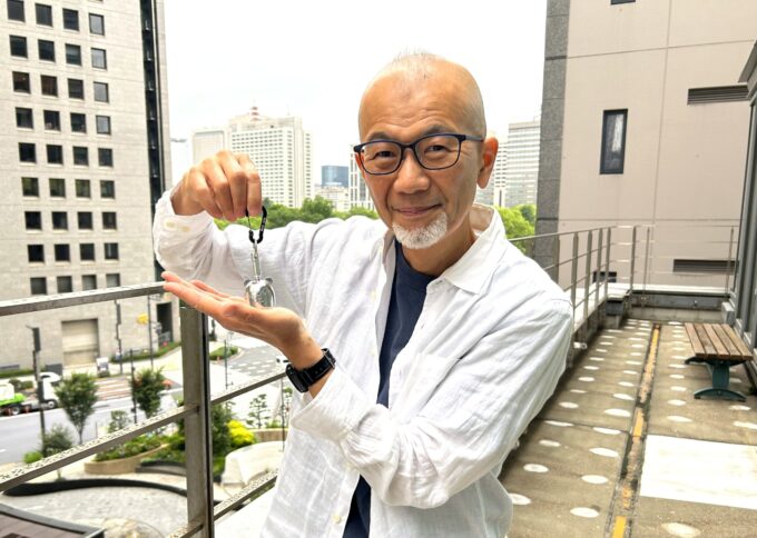 熊鈴をもつ上柳昌彦アナウンサー